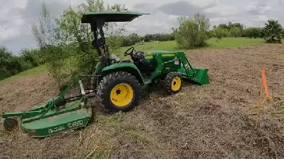 Picture of a landscape contractor using a John Deere tractor with a bushhog attachment to cut tall grass and brush